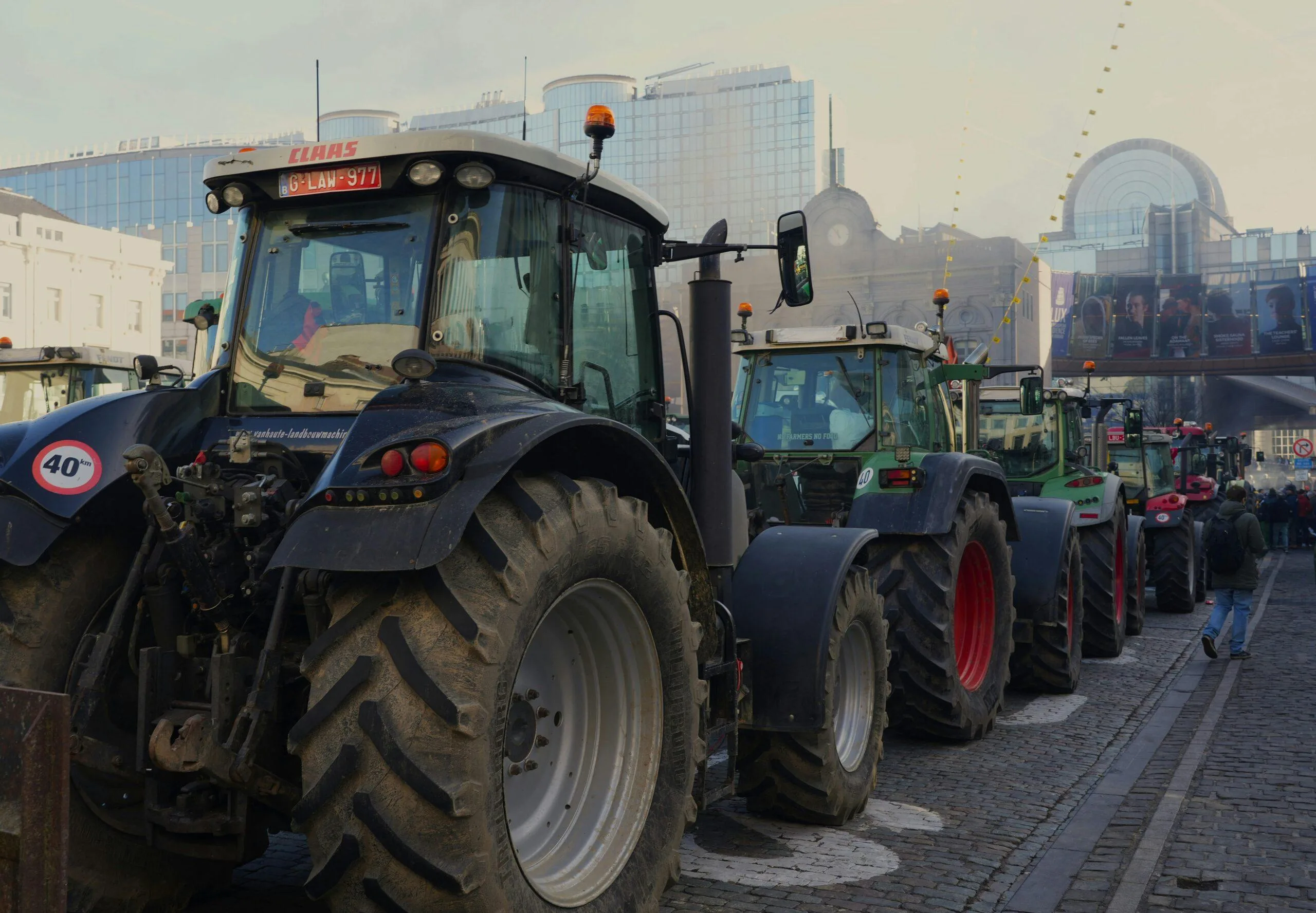 Row of tractors parked outdoors in a rural area with urban skyline in the background.